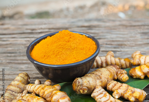Turmeric powder and fresh turmeric in black bowl on old wooden table background. herbal