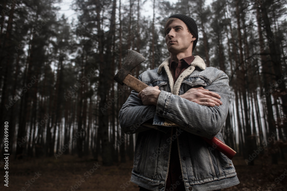 Strong lumberjack with the ax in the forest.Stylish lumberman getting ready for work. Lifestyle. Strong lumberjack with the ax in the forest.Stylish lumberman getting ready for work. Lifestyle.
