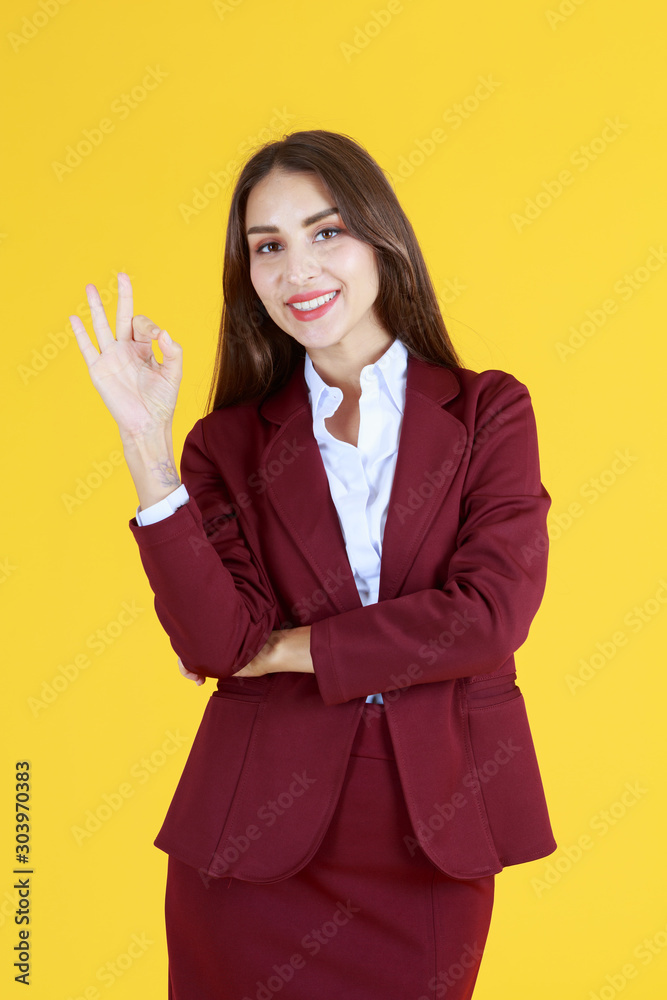 Beautiful woman in red dress showing right fingers OK symbol and gesture isolated on yellow background - working and business woman concept Beautiful woman in red dress showing right fingers OK symbol and gesture isolated on yellow background - working and business woman concept
