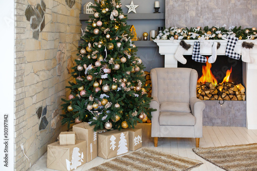 Stylish Christmas interior decorated in gray and beoge colors with fireplace. Comfort home in Christmas morning. Armchair with fabric upholstery. Craft handmade gift boxes