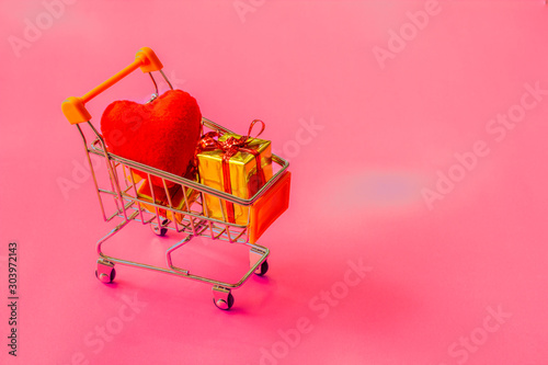 shopping cart full of gifts of different colors on a pink background, with a negative space