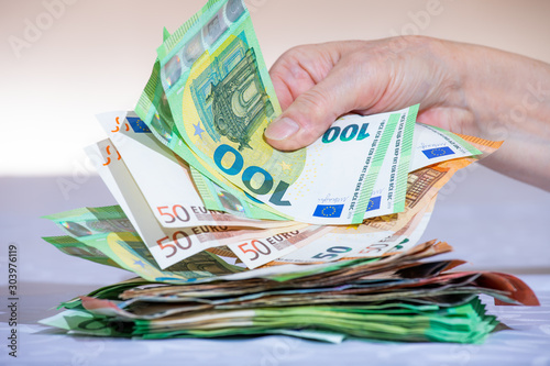 Photos A person's hand reaches for a large stack of bills lying on a table