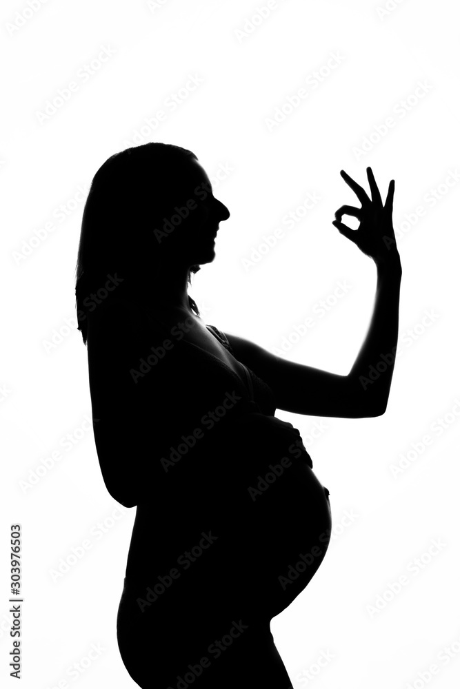 silhouette of a pregnant woman on a white background. The expectant mother shows the OK sign with her hands. The concept of a healthy lifestyle, IVF, expression of emotions, gestures. Copy space