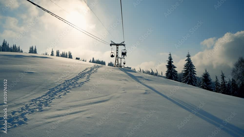 People moving up the snow mountains on ski elevator. Beautiful snowy forest landscape with tall fir trees covered with snow, sunset light. Winter adventure holiday and recreation on ski resort, styliz People moving up the snow mountains on ski elevator. Beautiful snowy forest landscape with tall fir trees covered with snow, sunset light. Winter adventure holiday and recreation on ski resort, styliz