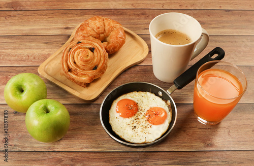 Ffried eggs , lattee coffee, orange juice ,croissant and danish pastry and two apples on wooden table.