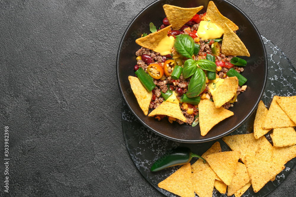Bowl with tasty chili con carne and nachos on dark background Bowl with tasty chili con carne and nachos on dark background