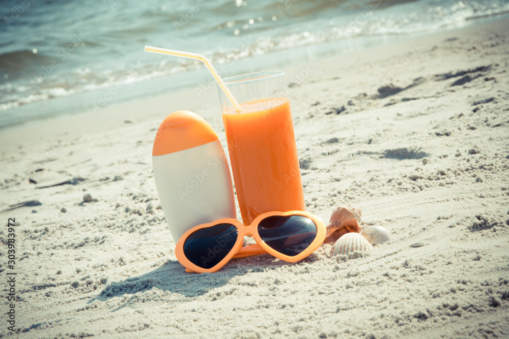 Carrot juice, sunglasses and sun lotion at beach, concept of vitamin A and beautiful, lasting tan Carrot juice, sunglasses and sun lotion at beach, concept of vitamin A and beautiful, lasting tan