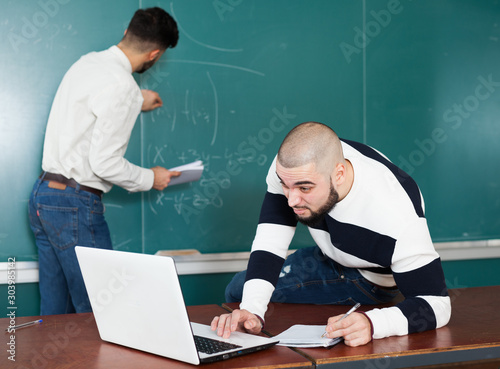 Students working with laptop near blackboard © JackF