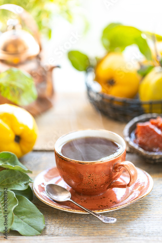 Cup of tea with homemade quince jam on an old wooden background. Fresh fruits and quince leaves on the background.