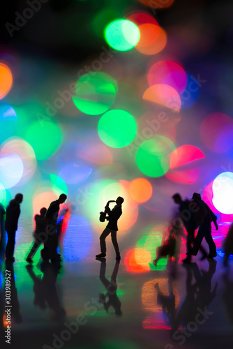 Miniature toy - Man blowing saxophone on the street with colorful bokeh lights among busy commuters crowd with colorful bokeh lights.