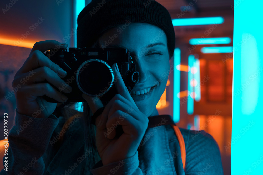 Smiling female photographer using camera in neon light - obrazy, fototapety, plakaty 