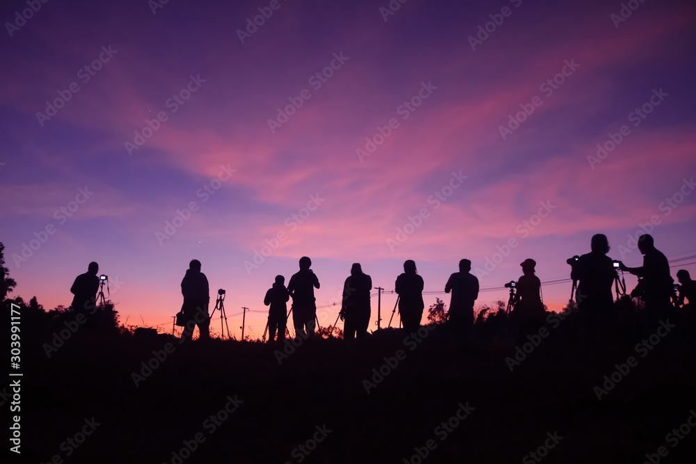 Many photographers taking pictures outdoors, silhouette of a man with camera over sunset