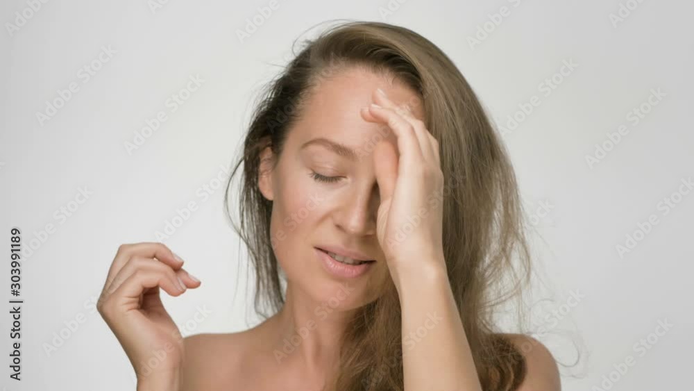 Close-up beauty portrait of young woman with smooth healthy skin, she gently touches hair with her hands and playfully looks at the camera on white background Close-up beauty portrait of young woman with smooth healthy skin, she gently touches hair with her hands and playfully looks at the camera on white background