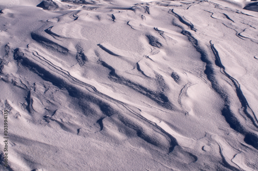 Fototapeta premium The surface of the snow cover in the light of the sun, with abstract patterns formed by the wind, a copy space, close-up, toned.