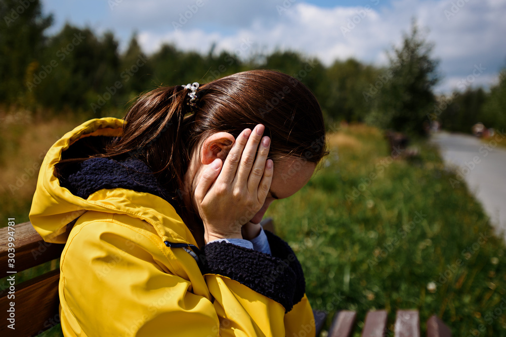 tired woman in yellow jacket sits on bench in state of stress
