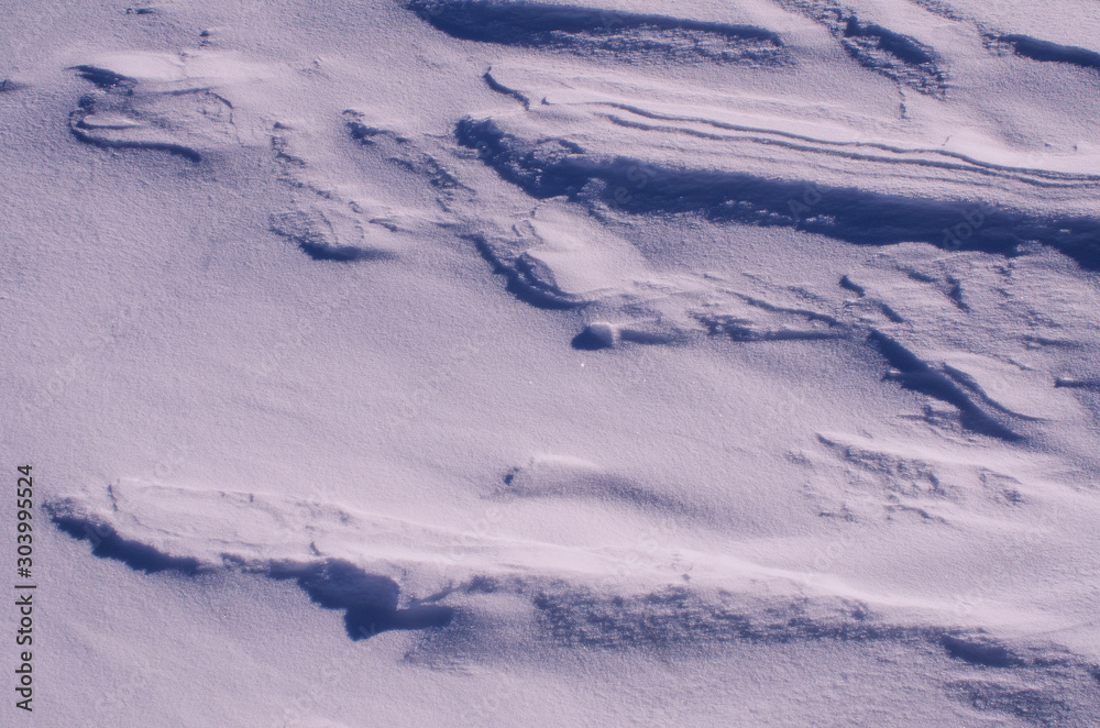 Fototapeta premium The surface of the snow cover in the light of the sun, with abstract patterns formed by the wind, a copy space, close-up, toned.