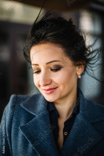 City portrait of beautiful young brunette woman in windy weather in blue coat.