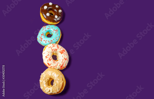 Set of assorted donuts with blue glaze, sprinkle, almond crumbs, chocolate and marshmallows close-up isolated on a purple background. Concept of sweet food (dessert).