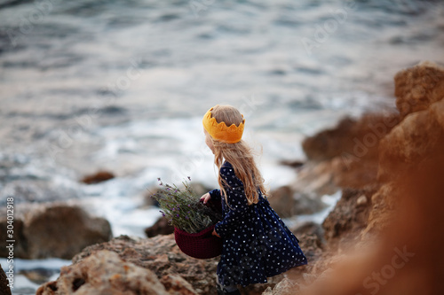 A pretty girl in a yellow knitted crown holds a basket of cord in her hands and stands on the seashore