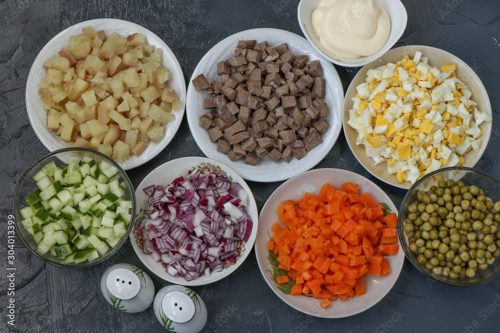 Ingredients for the preparation of Olivier salad: beef tongue, cucumbers, red onions, potatoes, carrots, eggs, canned peas and mayonnaise, top view Ingredients for the preparation of Olivier salad: beef tongue, cucumbers, red onions, potatoes, carrots, eggs, canned peas and mayonnaise, top view