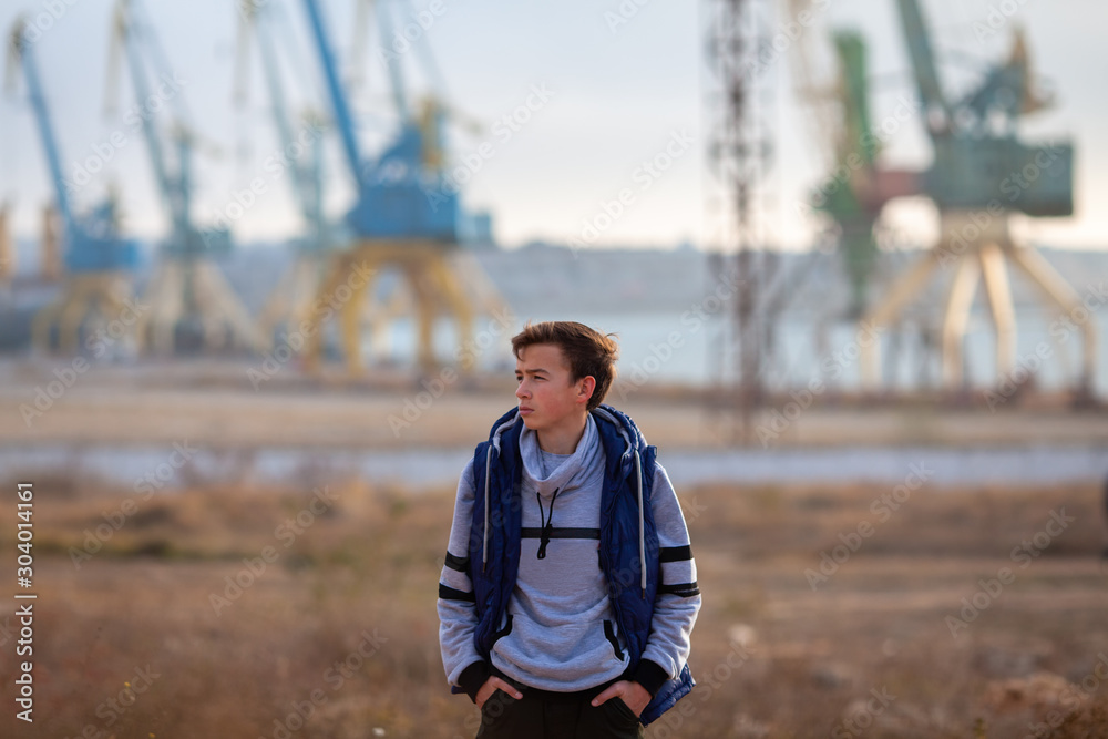 Naklejka premium Portrait of a handsome serious brutal guy. Teenager stands on the background of cranes