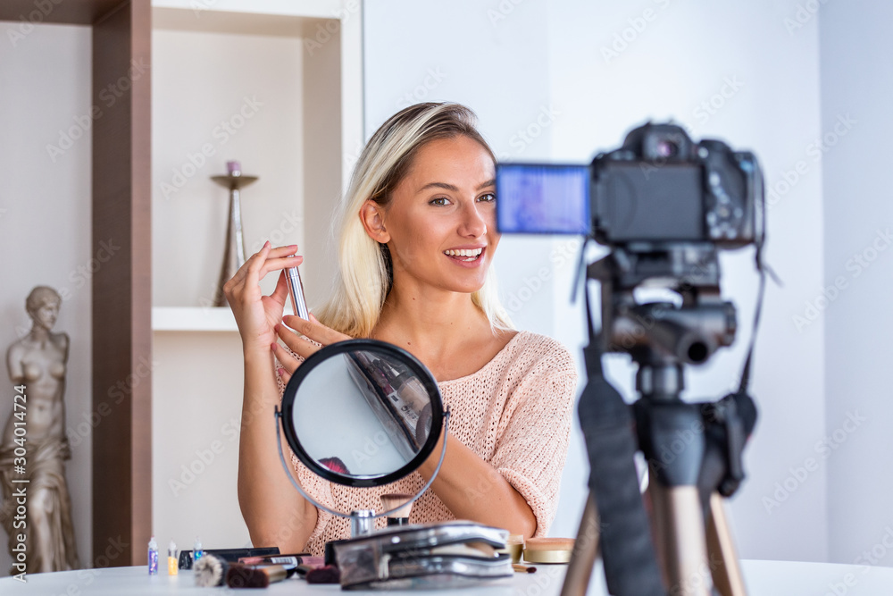 Young lady talking on cosmetics holding a makeup palette while recording her video. Woman making a video for her blog on cosmetics.