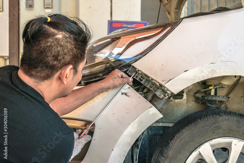a professional car mechanic is repairing a white modern vehicle after a road accident 
