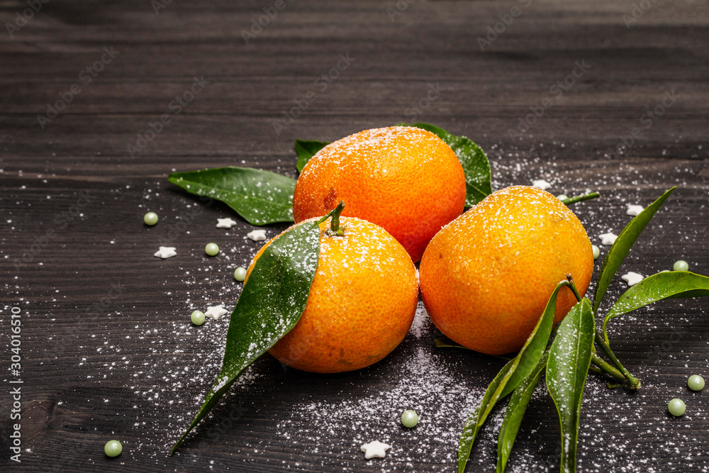 Fresh ripe tangerines with leaves and sprinkles. New Year or Christmas wooden background covered artificial snow. Festive good mood concept