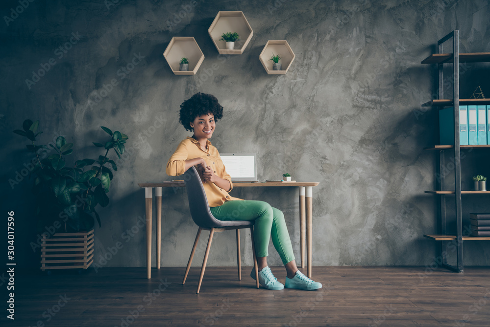 Full length photo of cool afro american girl college student sit table chair start work high-school presentation feel clever in office loft workstation wear yellow shirt green pants - obrazy, fototapety, plakaty 