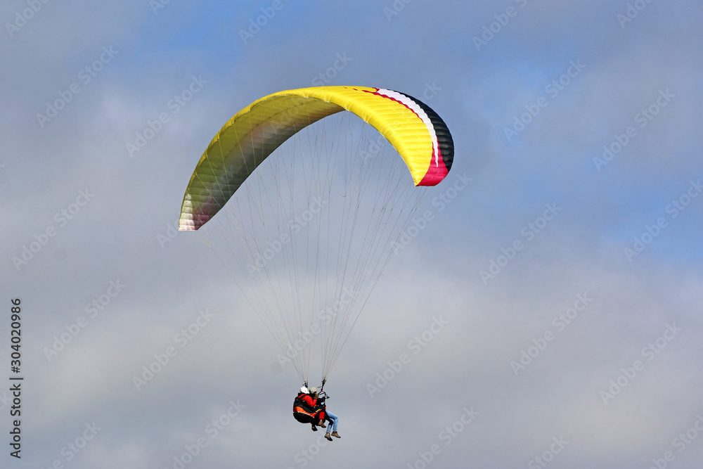 Tandem Paraglider flying wing in a cloudy sky Tandem Paraglider flying wing in a cloudy sky
