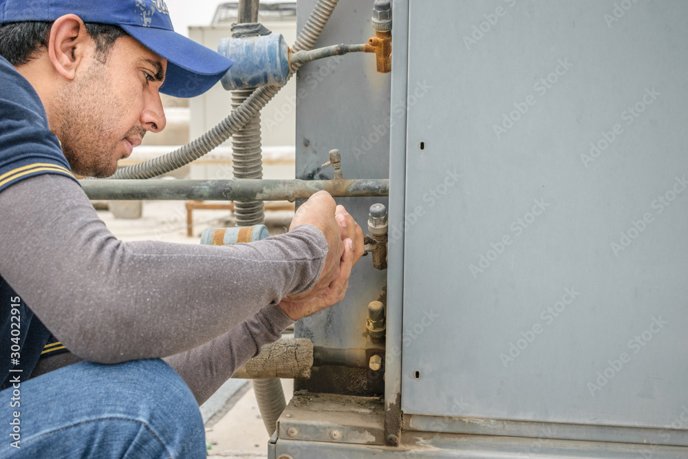 a professional electrician man is fixing the heavy unit of an air conditioner at the roof top of a building and wearing blue uniform and head cap a professional electrician man is fixing the heavy unit of an air conditioner at the roof top of a building and wearing blue uniform and head cap