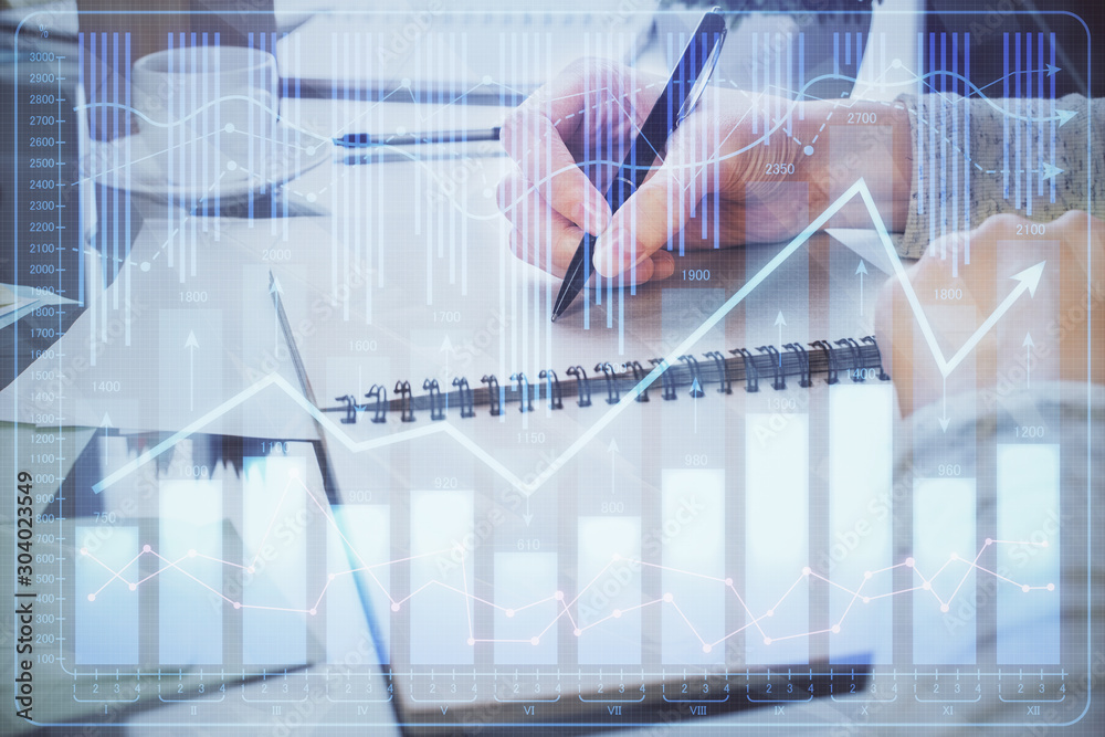 Hand taking notes in notepad. Forex chart holograms in front. Concept of research. Double exposure Hand taking notes in notepad. Forex chart holograms in front. Concept of research. Double exposure