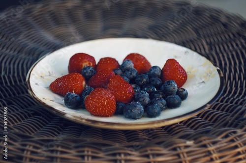 Blueberries and strawberries on ceramic plate. Wooden background. Fresh food vegan breakfast.