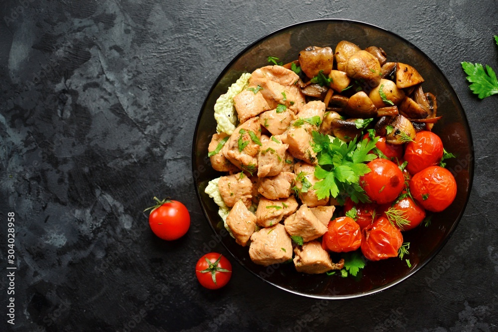 Tomatoes, chicken and mushrooms in a white plate on a dark background. Grilled tomatoes, fried champignons and grilled chicken. Vegetables and meat.