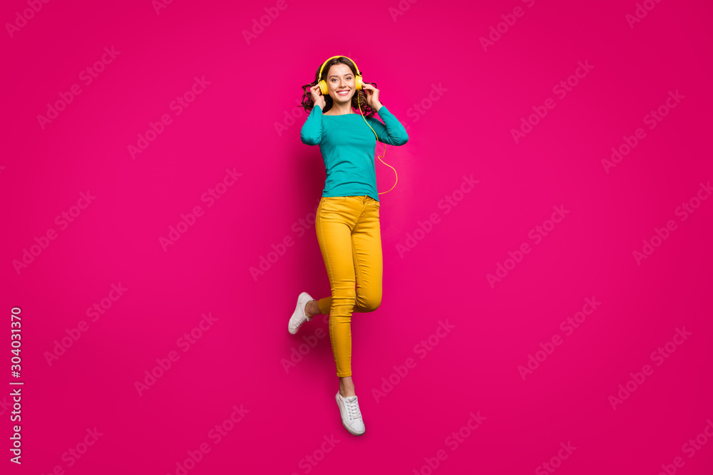 Full length body size photo of cheerful positive nice pretty cute charming girlfriend wearing yellow pants trousers white footwear smiling toothily isolated jumping over vivid pink color background
