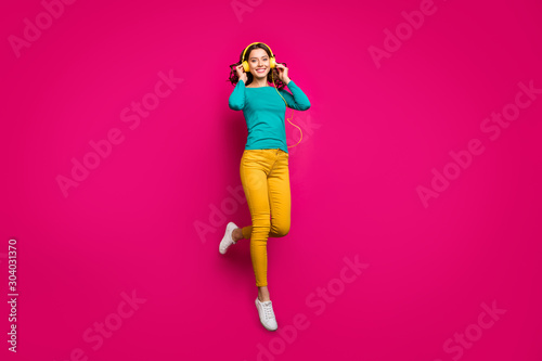 Full length body size photo of cheerful positive nice pretty cute charming girlfriend wearing yellow pants trousers white footwear smiling toothily isolated jumping over vivid pink color background