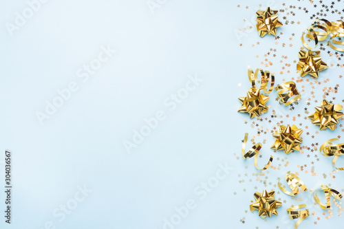 Flat lay background for celebration Christmas and New Year. gold ribbons bows and confetti stars on a blue background. top view copy space.