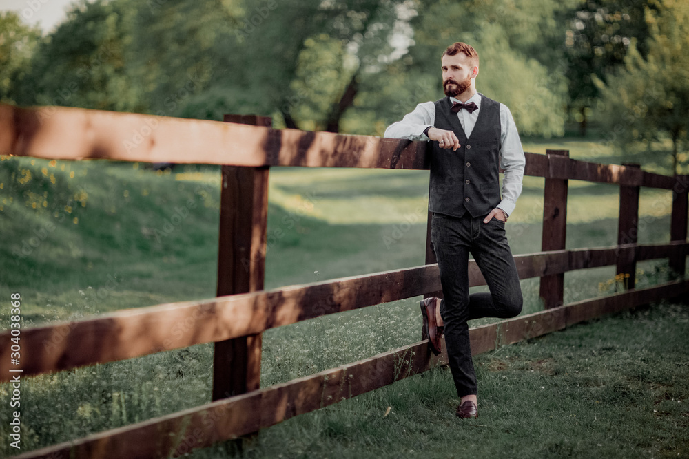 The bearded groom standing at the wooden fence.