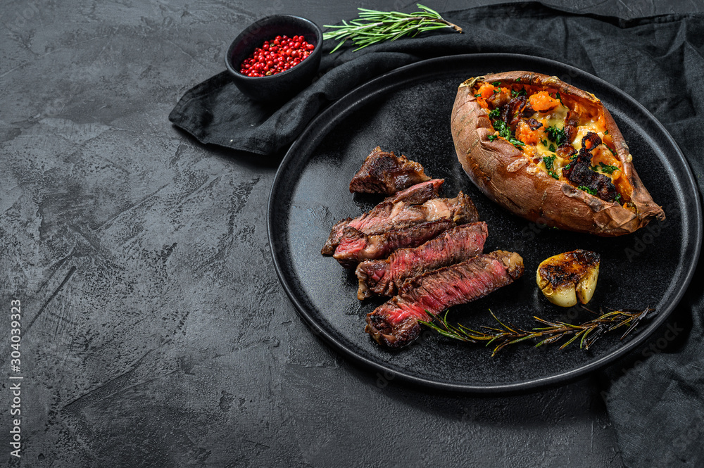 Marbled beef steak with baked sweet potato garnish. Grilled meat. Organic farm meat. Black background. Space for text.