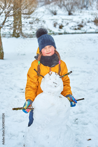 little girl sculpts a snowman in winter