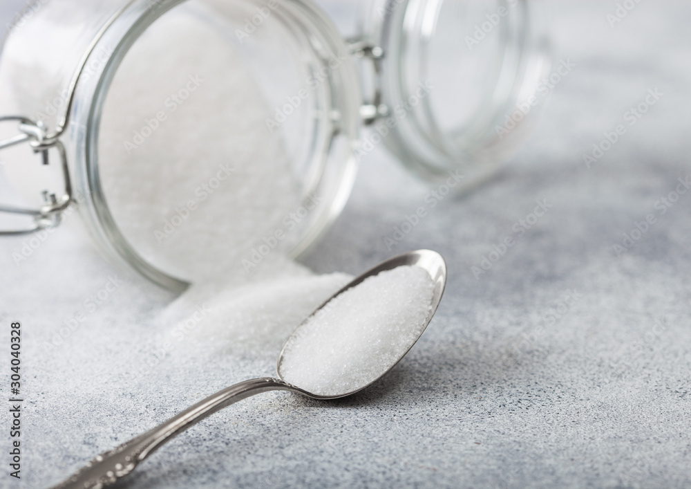 Glass jar of natural white refined sugar with silver spoon on light table background. - obrazy, fototapety, plakaty 