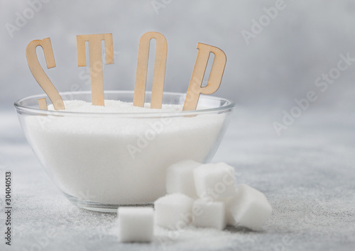 Glass bowl of natural white refined sugar with cubes on light table background with STOp letters. Unhealthy food concept.
