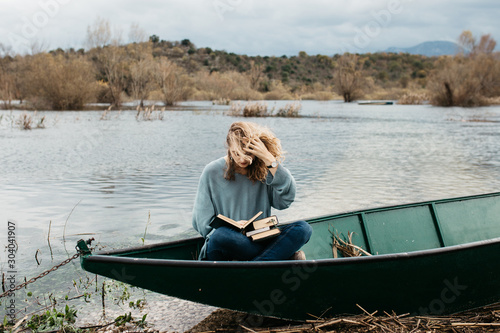 Portrait of young beautiful woman sitting on a boat and reading a book. She is bookworm and she choose between few books. 