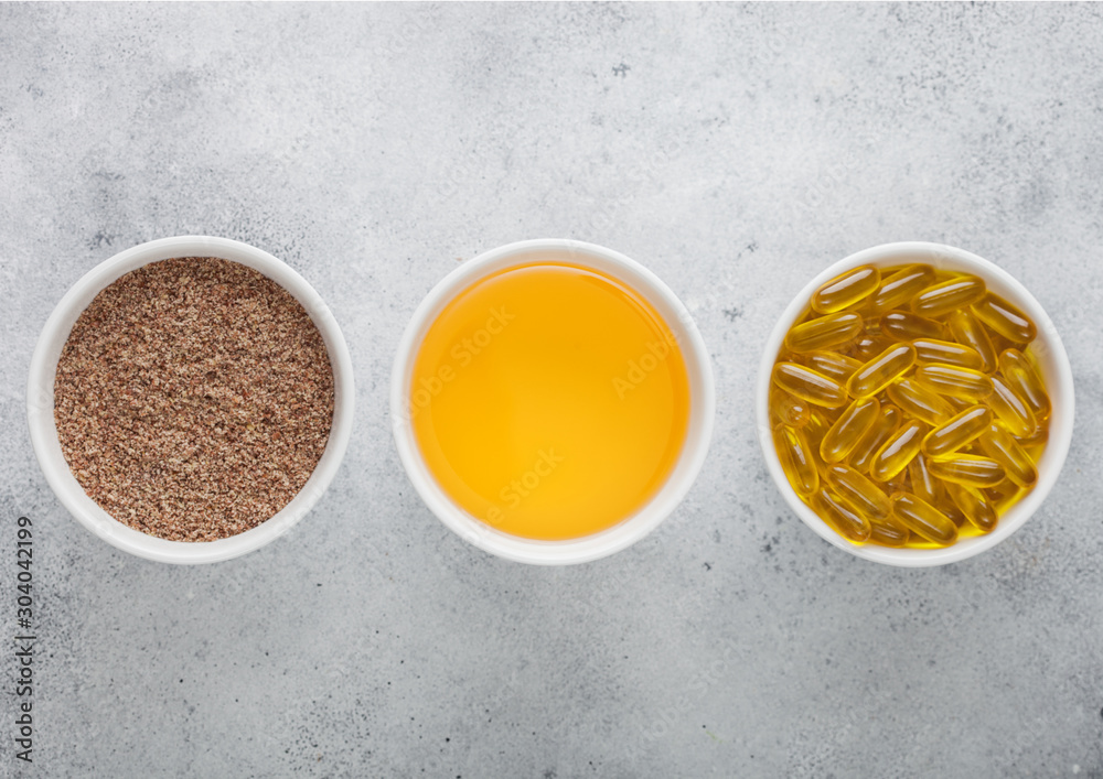Bowl of raw natural organic linseed flax-seed with oil and omega 3 capsules on light table background. Bowl of raw natural organic linseed flax-seed with oil and omega 3 capsules on light table background.