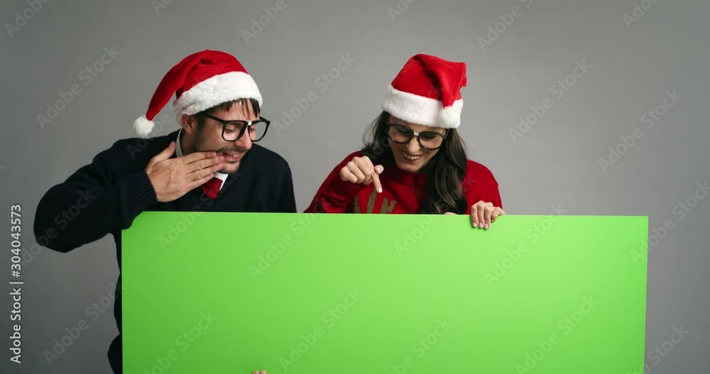 Nerd couple pointing on placard in Christmas clothes Nerd couple pointing on placard in Christmas clothes