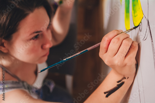 Female artist in her studio making a new masterpiece. Woman holding a brush drawing on the wall