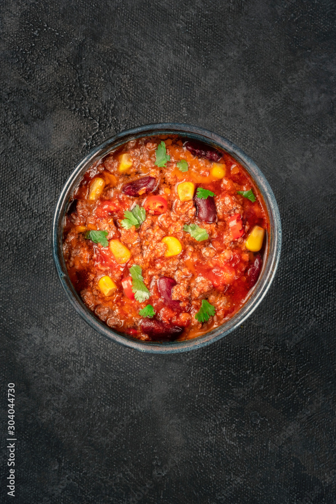Chili con carne, a Mexican stew with beans, ground meat, corn, and chilli peppers, overhead shot on a black background with a place for text Chili con carne, a Mexican stew with beans, ground meat, corn, and chilli peppers, overhead shot on a black background with a place for text