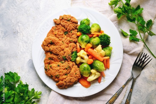 Chicken breast with vegetables. Baked chicken fillet, carrots, Brussels sprouts, broccoli, cauliflower. Food in a plate on a light wooden background.