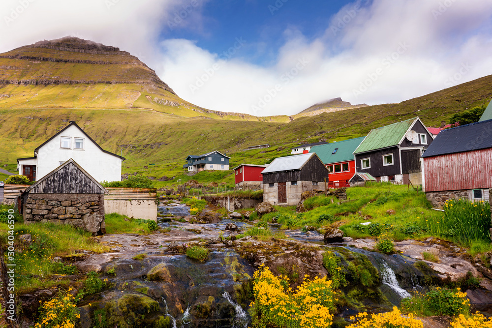 Colorful houses of Funningur village with a small river and outstanding mountains on background. Faroe Islands, Denmark.