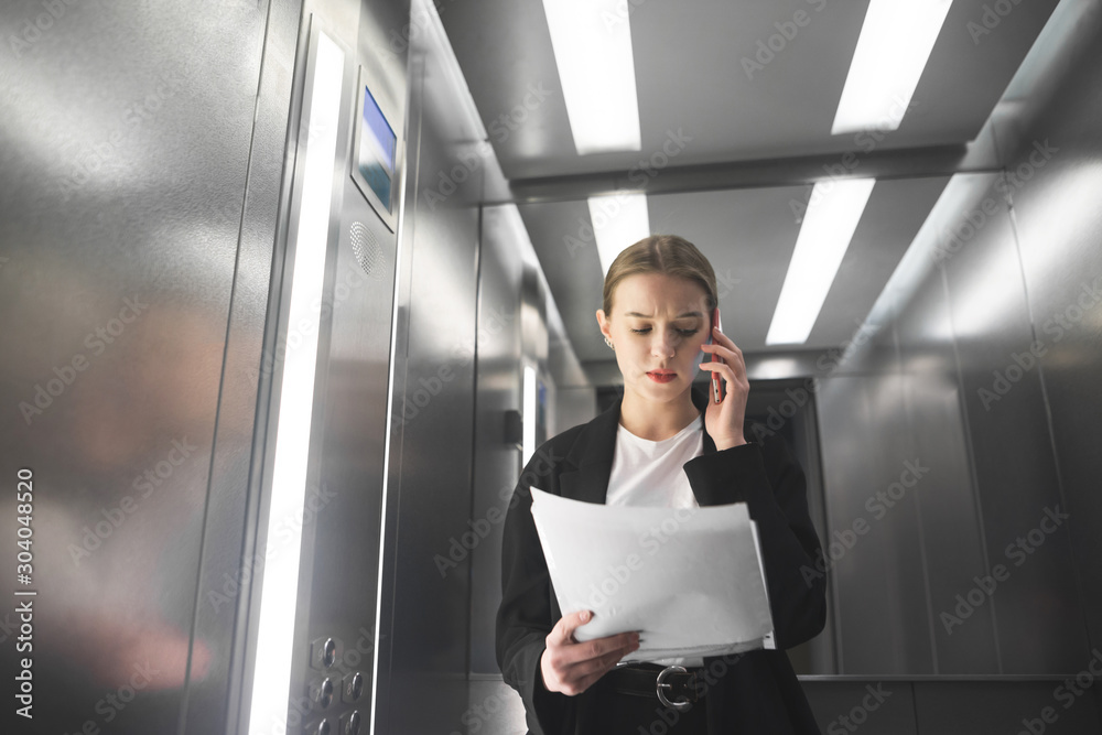 custom made wallpaper toronto digitalSerious businesswoman is talking by phone looking at papers in the elevator. Young female employee is reading the documents and talking by smartphone in the lift.